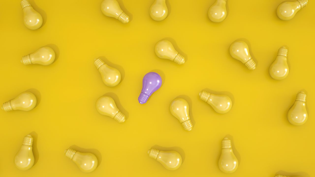 Standout purple light bulb among yellow bulbs on a yellow surface symbolizing individuality.