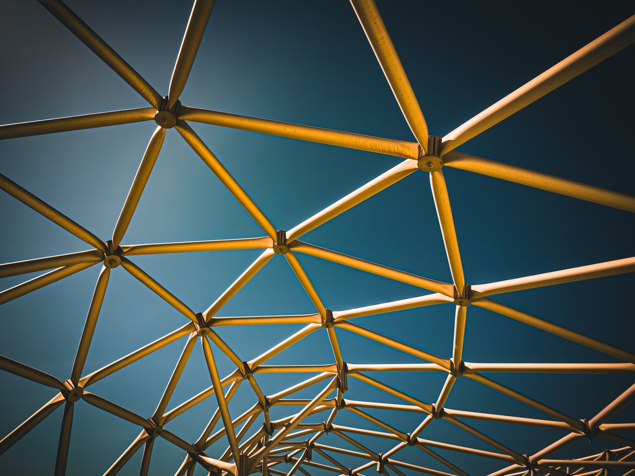 about-us Dynamic geometric metal structure with triangular patterns against a blue sky, showcasing modern architectural design.